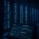 Futuristisches Rechenzentrum bei Nacht mit leuchtenden Serverracks, Bildschirm mit Performance-Diagrammen und Glasfassade, die die Serverräume zeigt