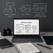Moderner Arbeitsplatz mit Laptop, Kamera, Grafiktablett und Notizbuch, im Hintergrund schematische Diagramme zu SEO-Strategien, sauber und professionell gestaltet.