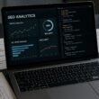 Nahaufnahme eines modernen Laptops mit SEO-Analyse-Dashboards, Diagrammen und Codeseiten, umgeben von Checklisten und technischen Schaltplänen auf einem Schreibtisch