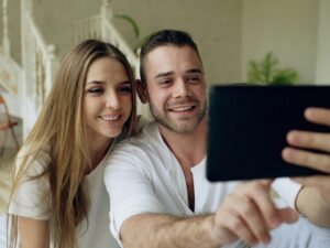 Ein Paar sitzt zusammen und nimmt ein Selfie mit einem Tablet auf, beide blicken in die Kamera des Geräts
