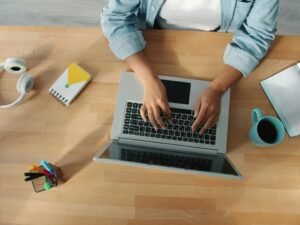 Person tippt auf einem Laptop an einem hölzernen Schreibtisch, detailreiche Ansicht der modernen Arbeitsweise
