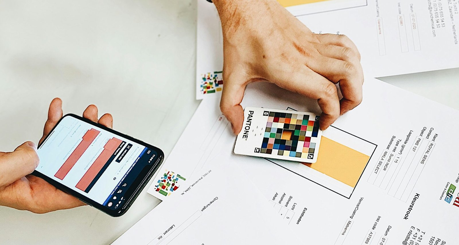 Person hält ein iPhone über weißem Druckerpapier, Symbol für mobile Technologie im Büroalltag