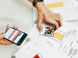 Person hält ein iPhone über weißem Druckerpapier, Symbol für mobile Technologie im Büroalltag