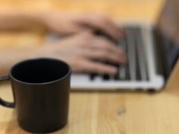 Eine Person arbeitet an einem MacBook Pro auf einem braunen Holztisch, Fokus auf Technik und Produktivität.