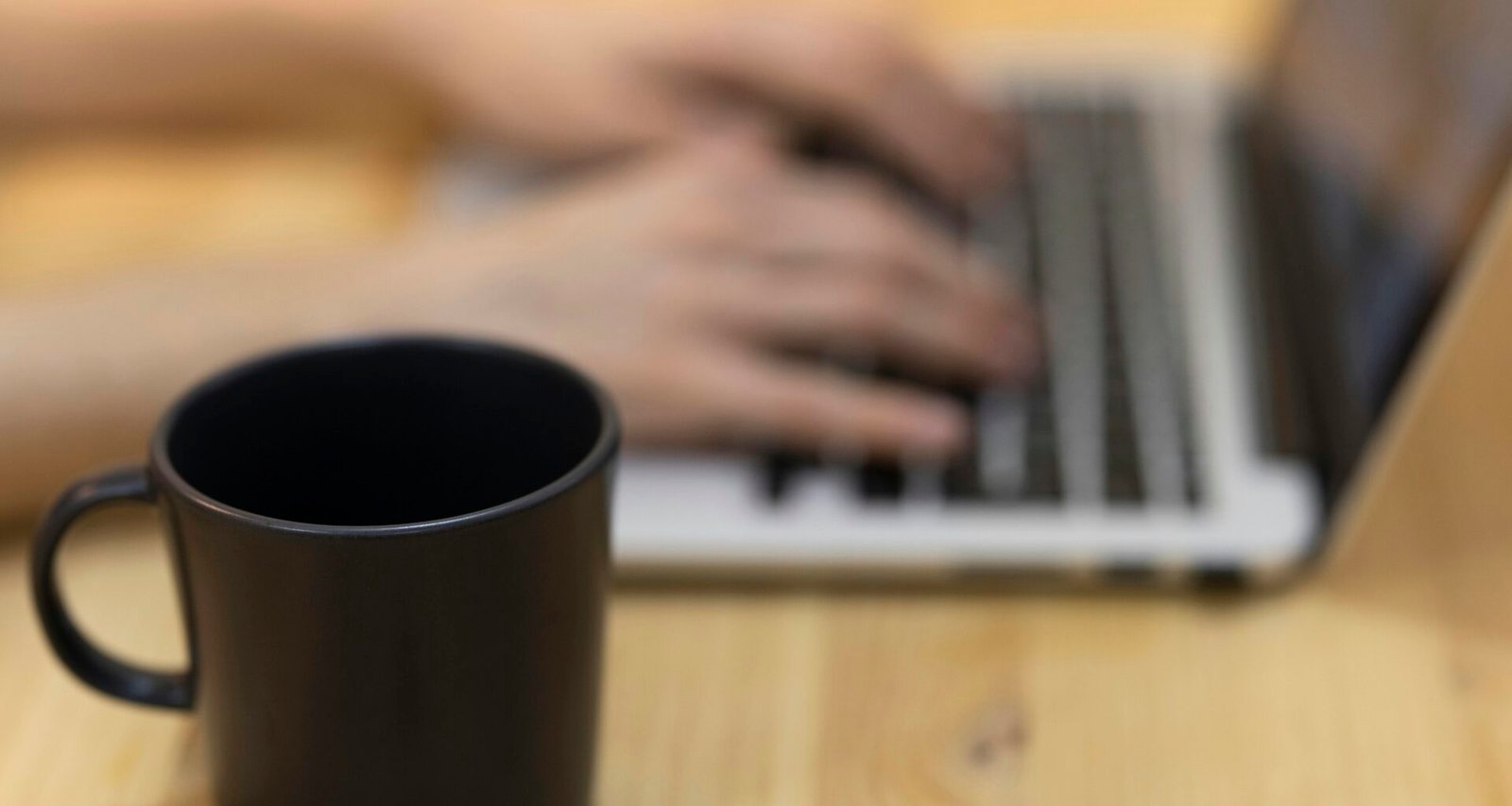 Person arbeitet mit einem MacBook Pro auf einem braunen Holztisch, bei natürlichem Licht in einem modernen Arbeitsumfeld.