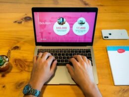 Person arbeitet mit einem MacBook Pro auf einem braunen Holztisch, moderne Arbeitsumgebung für digitale Aufgaben