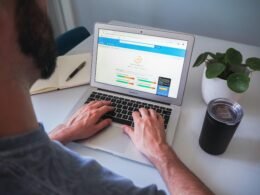 Eine Person arbeitet an einem MacBook Pro auf einem weißen Tisch in einer modernen Büro-Umgebung.