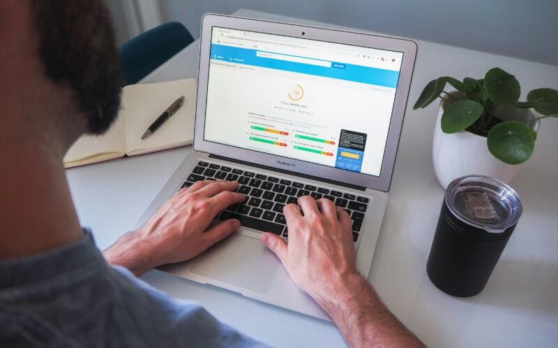 Person arbeitet mit einem MacBook Pro auf einem weißen Tisch in einer modernen, hellen Büro-Umgebung