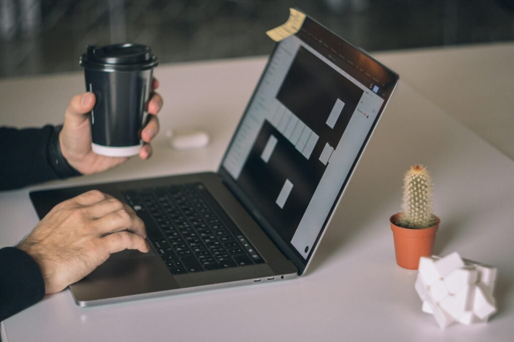Person arbeitet an einem MacBook Pro auf weißem Tisch in moderner Arbeitsumgebung mit Fokus auf Technologieeinsatz.