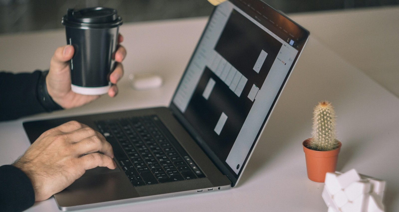 Person arbeitet an einem MacBook Pro auf weißem Tisch in moderner Arbeitsumgebung mit Fokus auf Technologieeinsatz.