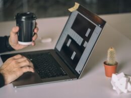 Person arbeitet an einem MacBook Pro auf weißem Tisch in moderner Arbeitsumgebung mit Fokus auf Technologieeinsatz.