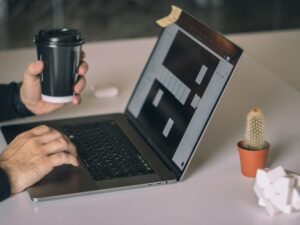 Person arbeitet an einem MacBook Pro auf weißem Tisch in moderner Arbeitsumgebung mit Fokus auf Technologieeinsatz.