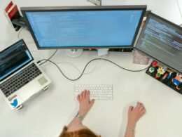 Person arbeitet konzentriert an einem MacBook Pro auf einem weißen Tisch im modernen Arbeitsumfeld.