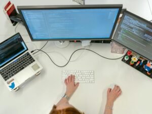 Person arbeitet an einem MacBook Pro auf einem weißen Tisch, digitale Arbeitsumgebung mit moderner Technik