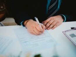Eine Person unterschreibt ein wichtiges Dokument mit einem Kugelschreiber an einem Tisch im Büro.
