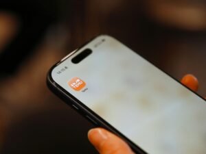 Eine Person hält ein Smartphone in der Hand, auf dem ein farbiges App-Symbol auf dem Display zu sehen ist.