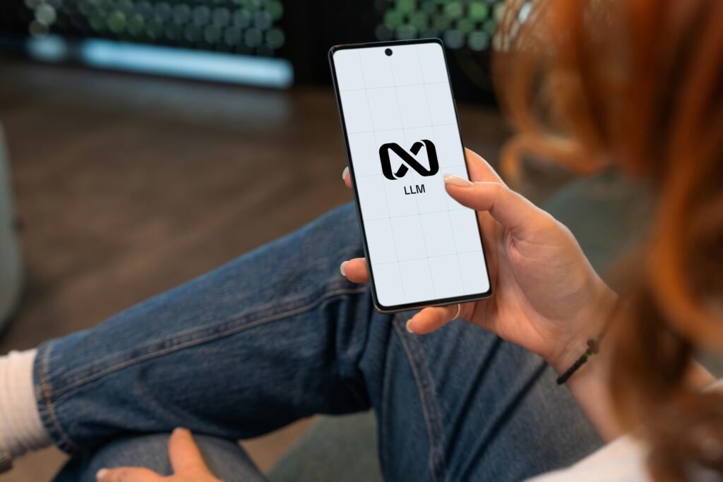 Person hält ein Smartphone mit Logo auf dem Display, Fokus auf die Hand und den Bildschirm, neutraler Hintergrund