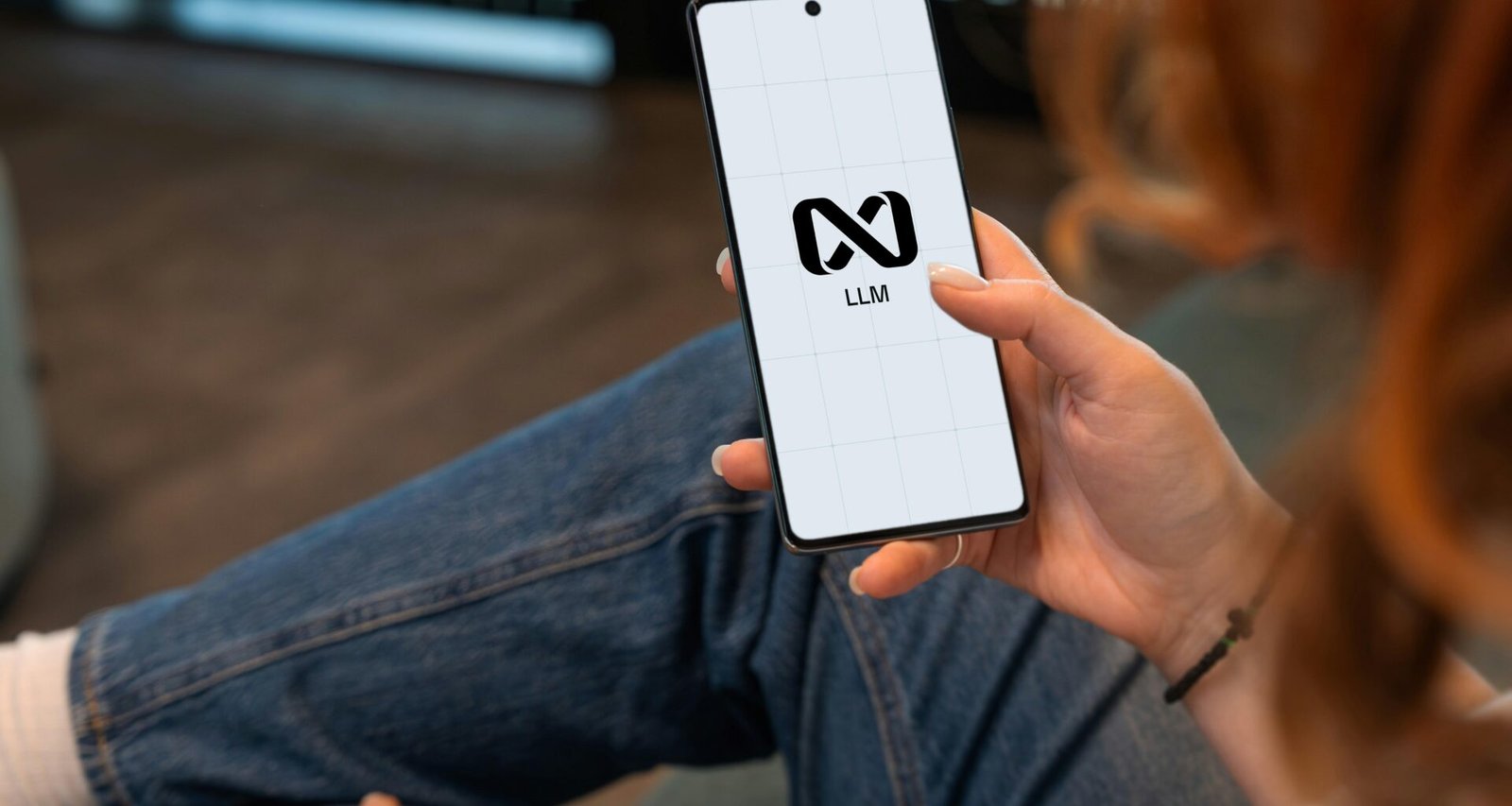 Person hält ein Smartphone mit Logo auf dem Display, Fokus auf die Hand und den Bildschirm, neutraler Hintergrund