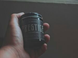 Person hält eine Prestige Flasche in der Hand, neutraler Hintergrund, Fokus auf Produktdesign und Markenpräsenz.