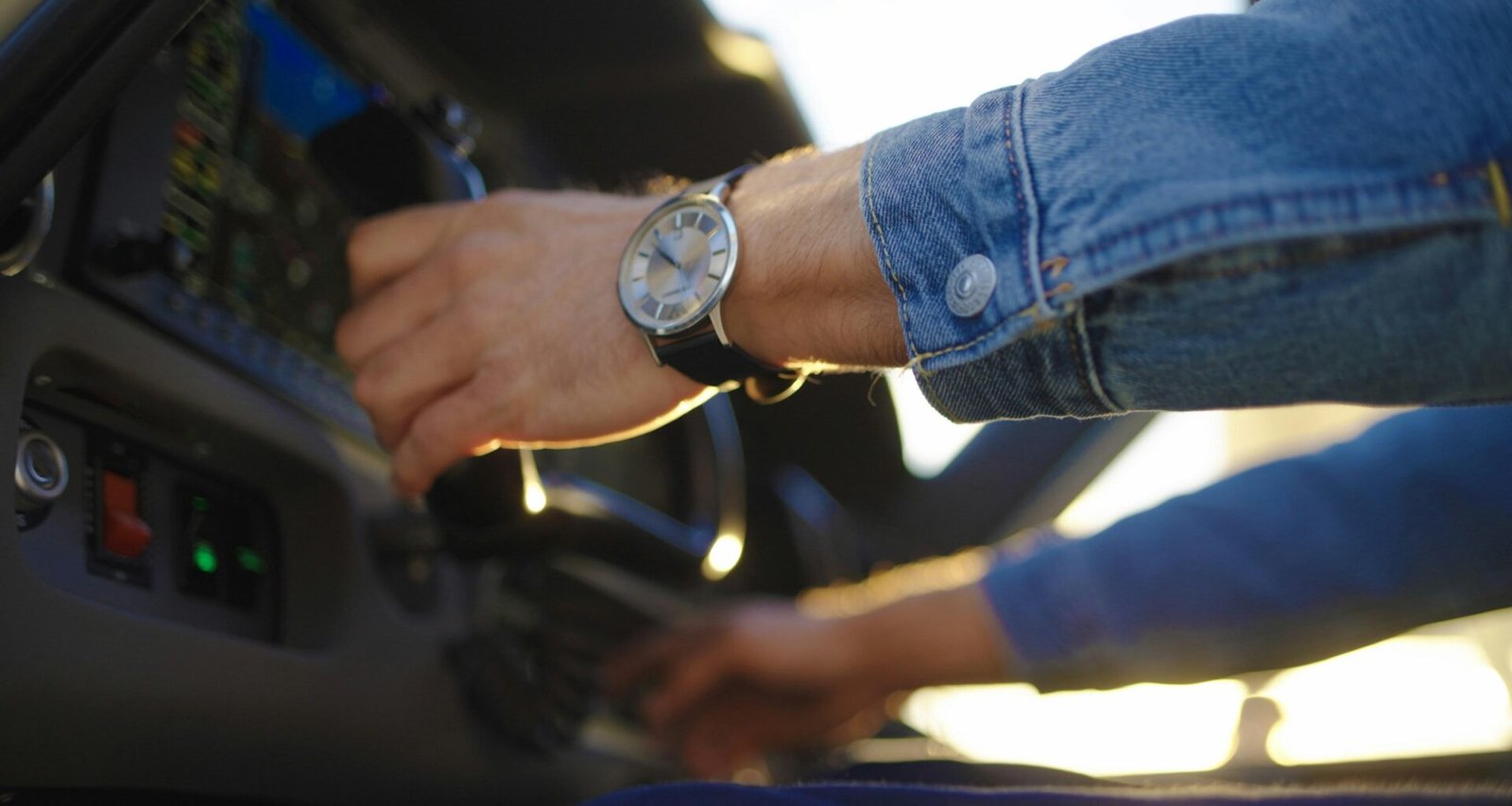 Person mit Armbanduhr startet ein Fahrzeug, Fokus auf Hand, Uhr und Zündschlüssel im Innenraum des Autos.