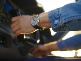 Person mit Armbanduhr startet ein Fahrzeug, Fokus auf Hand, Uhr und Zündschlüssel im Innenraum des Autos.