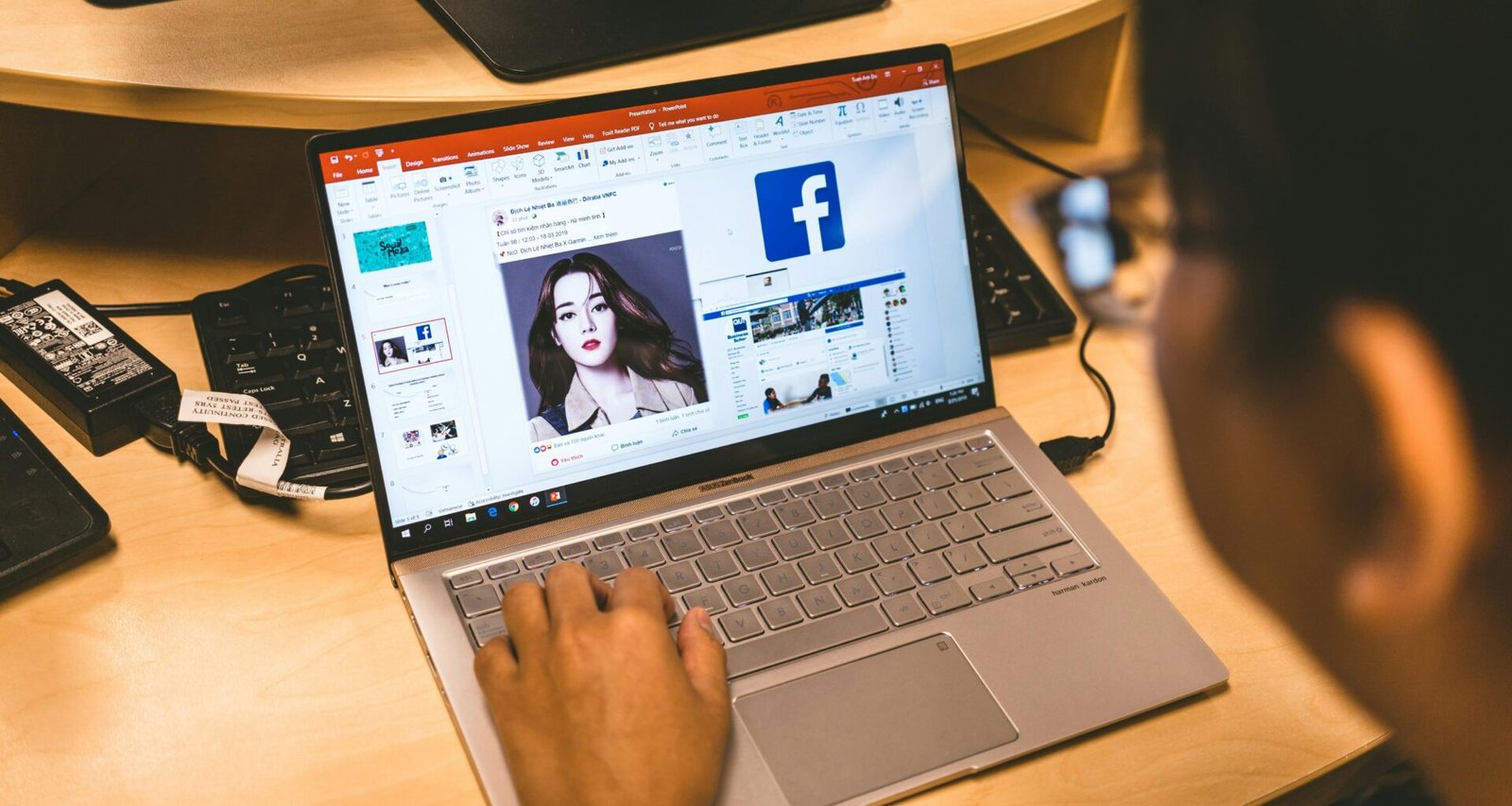 Person sitzt an einem Tisch und verwendet ihren Laptop, um durch die Facebook-Anwendung im Browser zu navigieren.