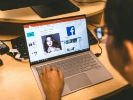 Person sitzt an einem Tisch und verwendet ihren Laptop, um durch die Facebook-Anwendung im Browser zu navigieren.