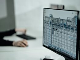 Person sitzt an einem Tisch und verwendet ein schwarzes Laptop, Fokus auf Technik und Arbeitssituation