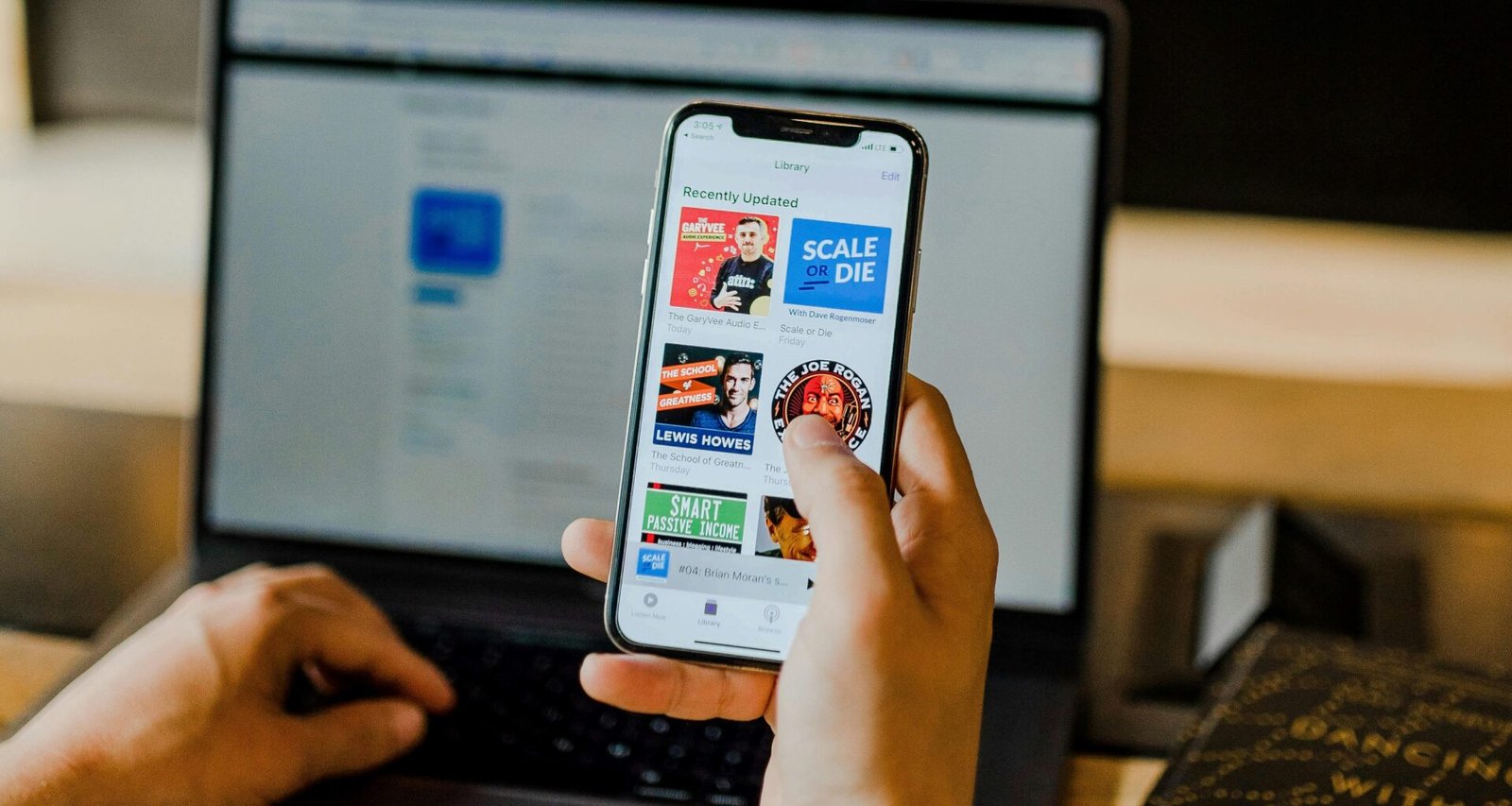 Person sitzt an einem Tisch und nutzt gleichzeitig ein Smartphone und einen Laptop für Arbeit oder Kommunikation