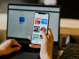 Person sitzt an einem Tisch und nutzt gleichzeitig ein Smartphone und einen Laptop für Arbeit oder Kommunikation