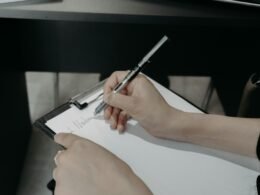 Person schreibt mit einem Stift auf ein Clipboard, festhaltend wichtige Informationen oder Aufgaben.