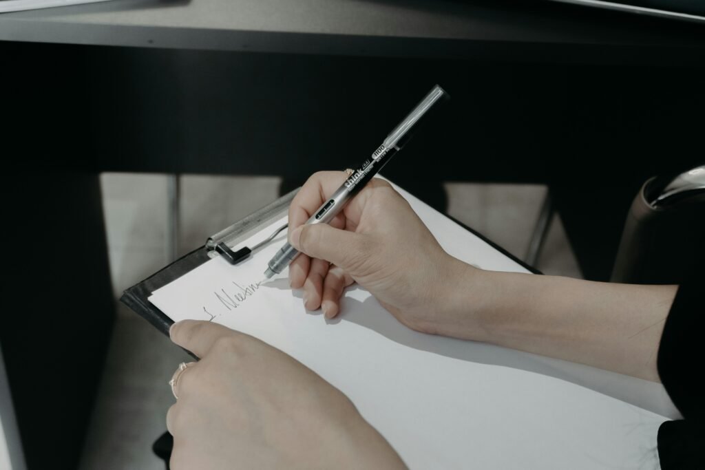 Person schreibt mit einem Stift auf ein Clipboard und hält Notizen fest. Das Bild symbolisiert Organisation und Planung.