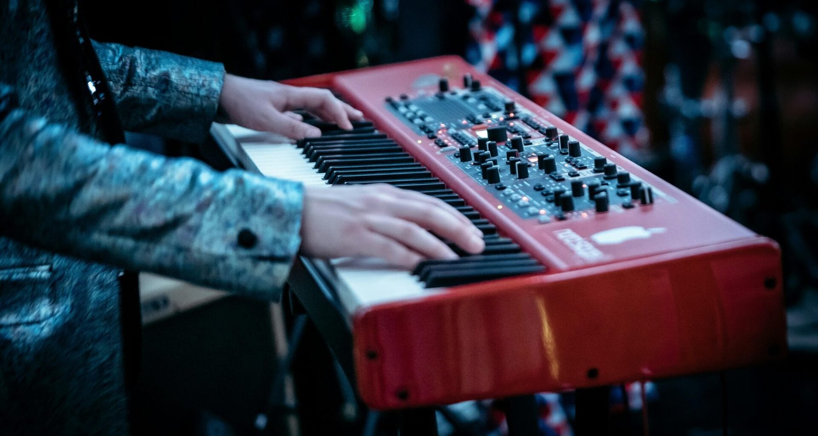 Person spielt auf einem rot-weißen Klavier in modernem Design, Fokus auf den Händen auf den Tasten.