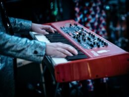 Person spielt auf einem rot-weißen Klavier in modernem Design, Fokus auf den Händen auf den Tasten.