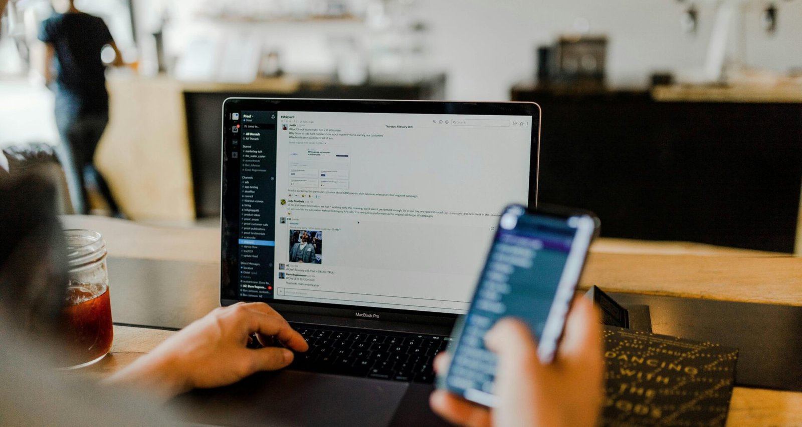 Person sitzt am Tisch und nutzt gleichzeitig ein Smartphone und einen Laptop zum Arbeiten.