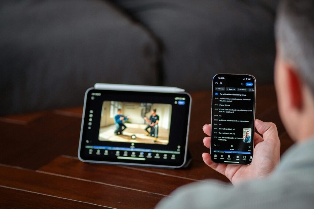 Eine Person sieht sich ein Video gleichzeitig auf einem Tablet und einem Smartphone an, Geräte liegen auf einem Holztisch.