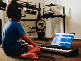 Eine Person mit blauem Hemd sitzt an einem Klavier und spielt, Fokus liegt auf den Händen auf den Tasten.