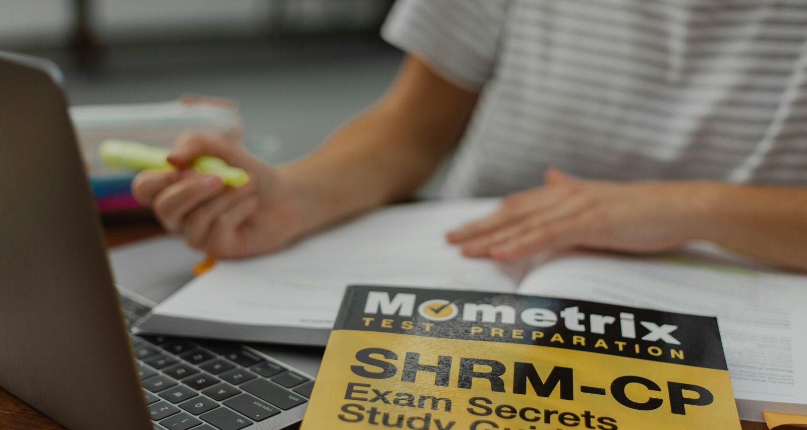 Person in grauem Shirt arbeitet an einem MacBook Pro an einem Schreibtisch. Die Arbeitsumgebung wirkt aufgeräumt und modern.