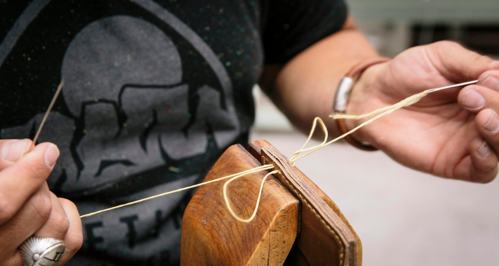Person im schwarzen T-Shirt hält ein braunes Holz-Gitarrenplektrum zwischen den Fingern, Fokus auf Hand und Plektrum