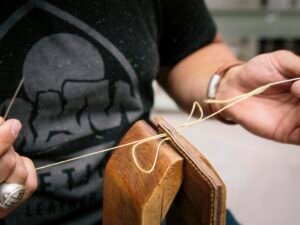 Person im schwarzen T-Shirt hält ein braunes Holz-Gitarrenplektrum zwischen den Fingern, Fokus auf Hand und Plektrum