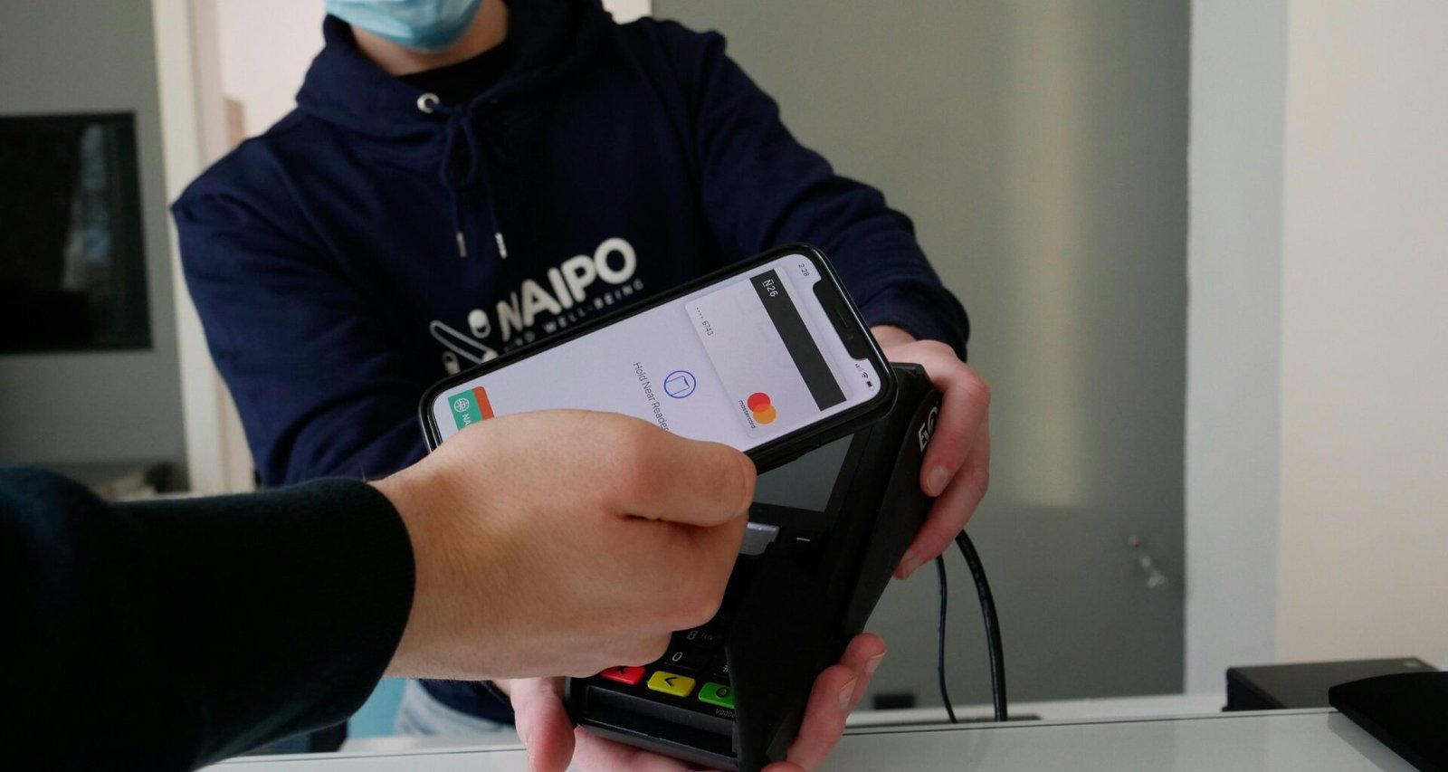 Person trägt einen schwarz-weißen Nike-Hoodie und hält ein schwarzes iPhone 4 in der Hand vor neutralem Hintergrund