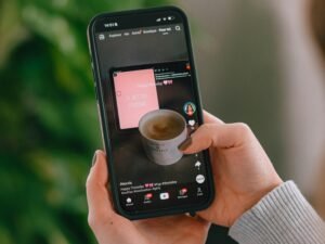 Person hält ein Smartphone, auf dem eine Kaffeetasse auf dem Bildschirm angezeigt wird, Nahaufnahme der Hand mit Handy