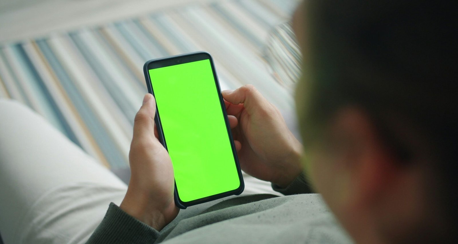 Person hält ein Smartphone mit grünem Bildschirm in der Hand, geeignet für Themen rund um mobile Technologien oder App-Entwicklung.