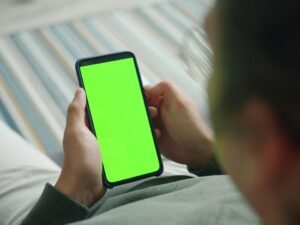 Person hält ein Smartphone mit grünem Bildschirm in der Hand, geeignet für Themen rund um mobile Technologien oder App-Entwicklung.