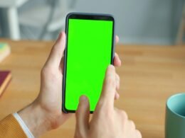 Person zeigt ein Smartphone mit leuchtend grünem Bildschirm – ideal für Themen rund um mobile Technologie und digitale Anwendungen.