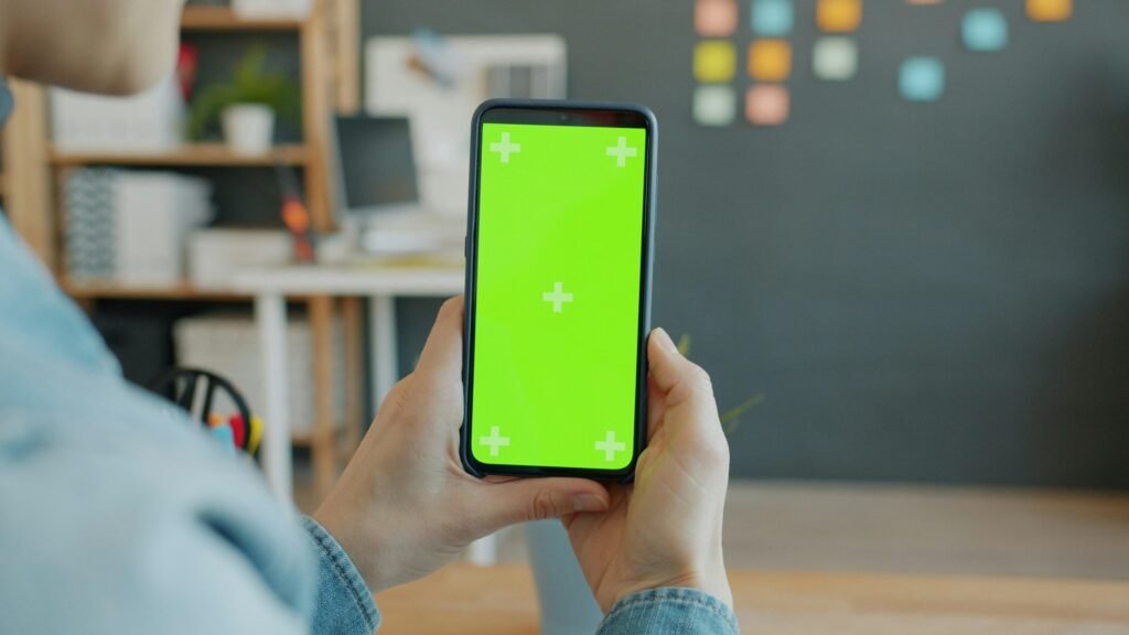 Eine Person hält ein Smartphone mit grünem Bildschirm, ideal für Technik- oder App-Darstellungen in Online-Artikeln.