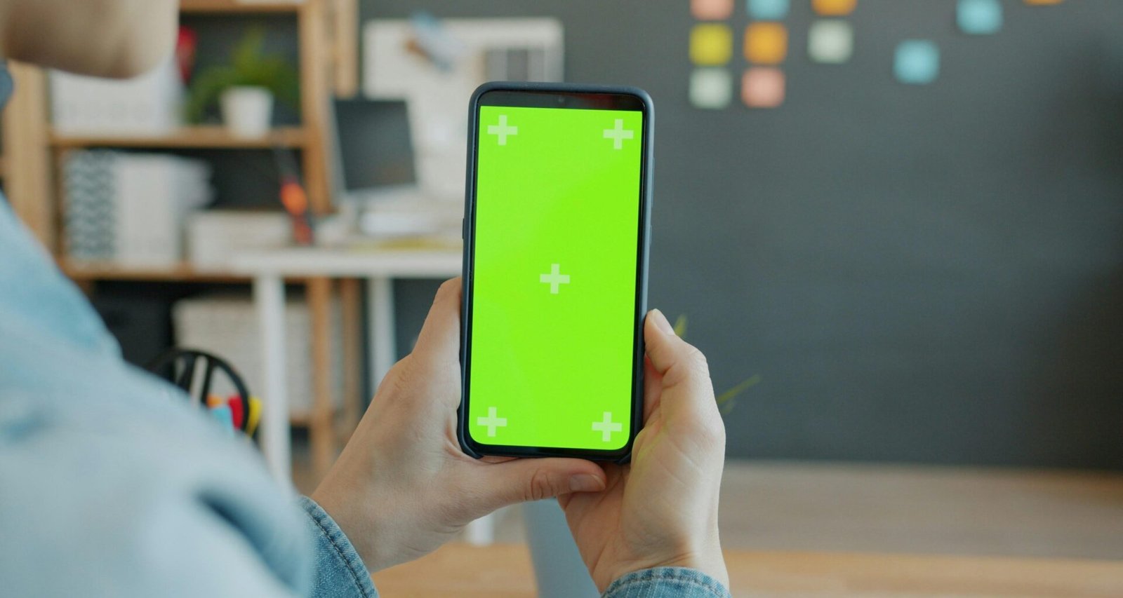 Eine Person hält ein Smartphone mit grünem Bildschirm, ideal für Technik- oder App-Darstellungen in Online-Artikeln.
