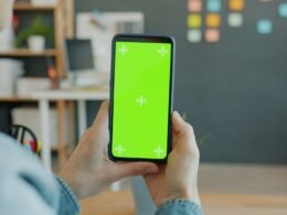 Eine Person hält ein Smartphone mit grünem Bildschirm, ideal für Technik- oder App-Darstellungen in Online-Artikeln.
