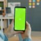 Eine Person hält ein Smartphone mit grünem Bildschirm, ideal für Technik- oder App-Darstellungen in Online-Artikeln.