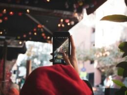 Eine Person hält ein eingeschaltetes schwarzes Smartphone in der Hand, Fokus auf das Gerät und die Nutzung im Alltag